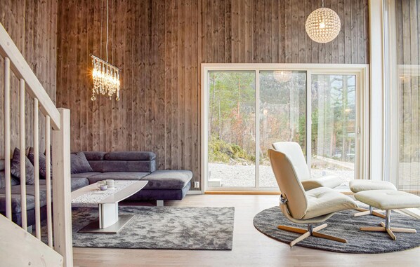 Una sala de estar moderna con pared de madera, un ventanal grande, un sofá gris, un sillón blanco y una lámpara colgante.