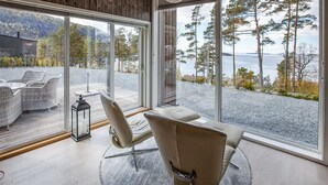 Une chambre moderne dotée d’une grande fenêtre donnant sur un espace extérieur agréable, avec des arbres et une étendue d’eau.
