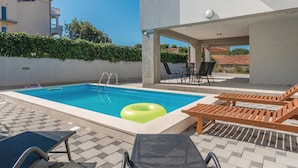 Ein Schwimmbecken mit einem grünen Schwimmreifen, Liegestühlen und einem Tisch mit Stühlen.