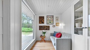 A room with a wooden floor, a grey sofa with a red pillow, a small wooden table with a vase of flowers, and a cabinet with glass doors.