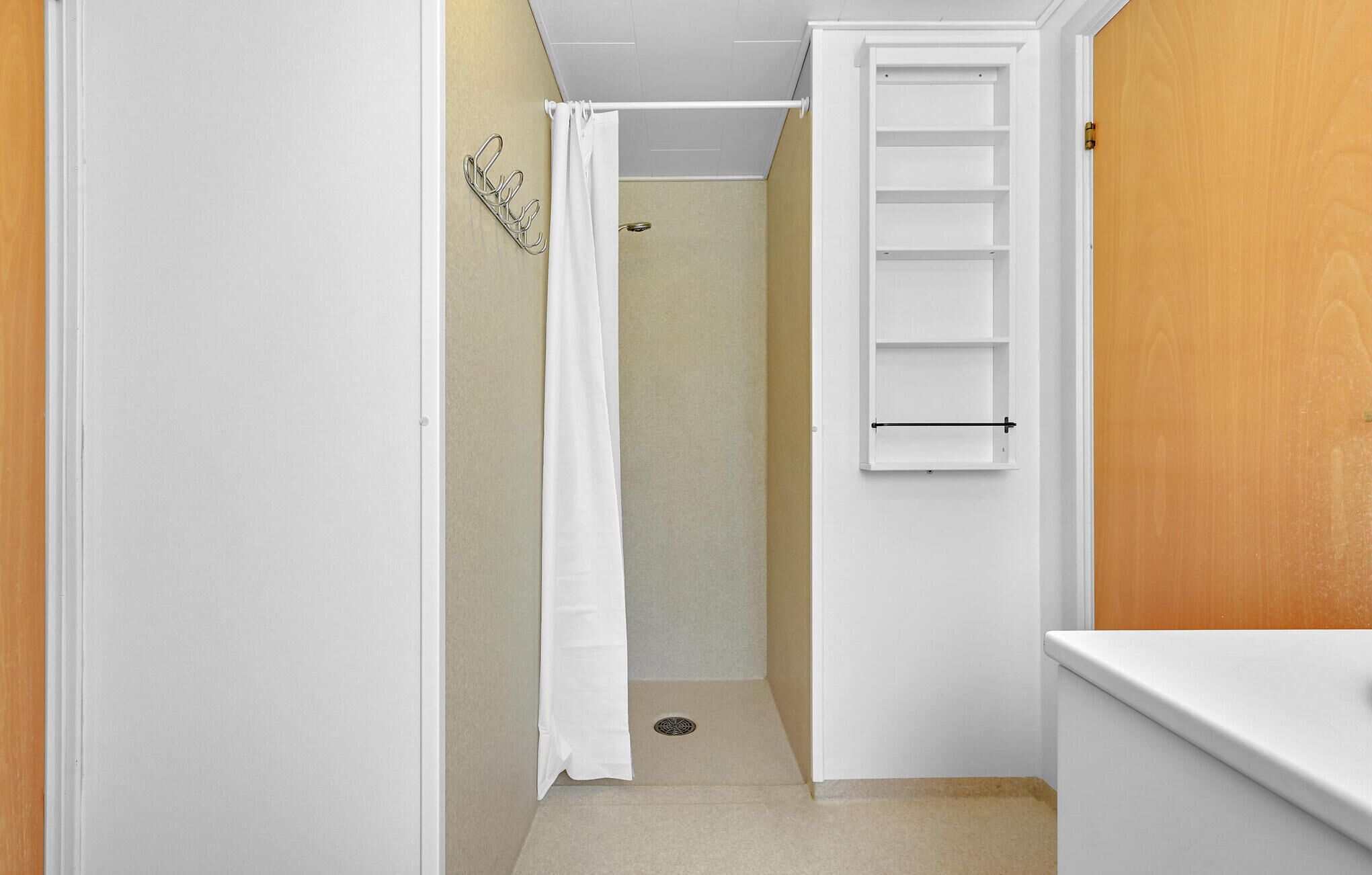 Un baño estrecho con ducha, un perchero blanco y una puerta de madera.