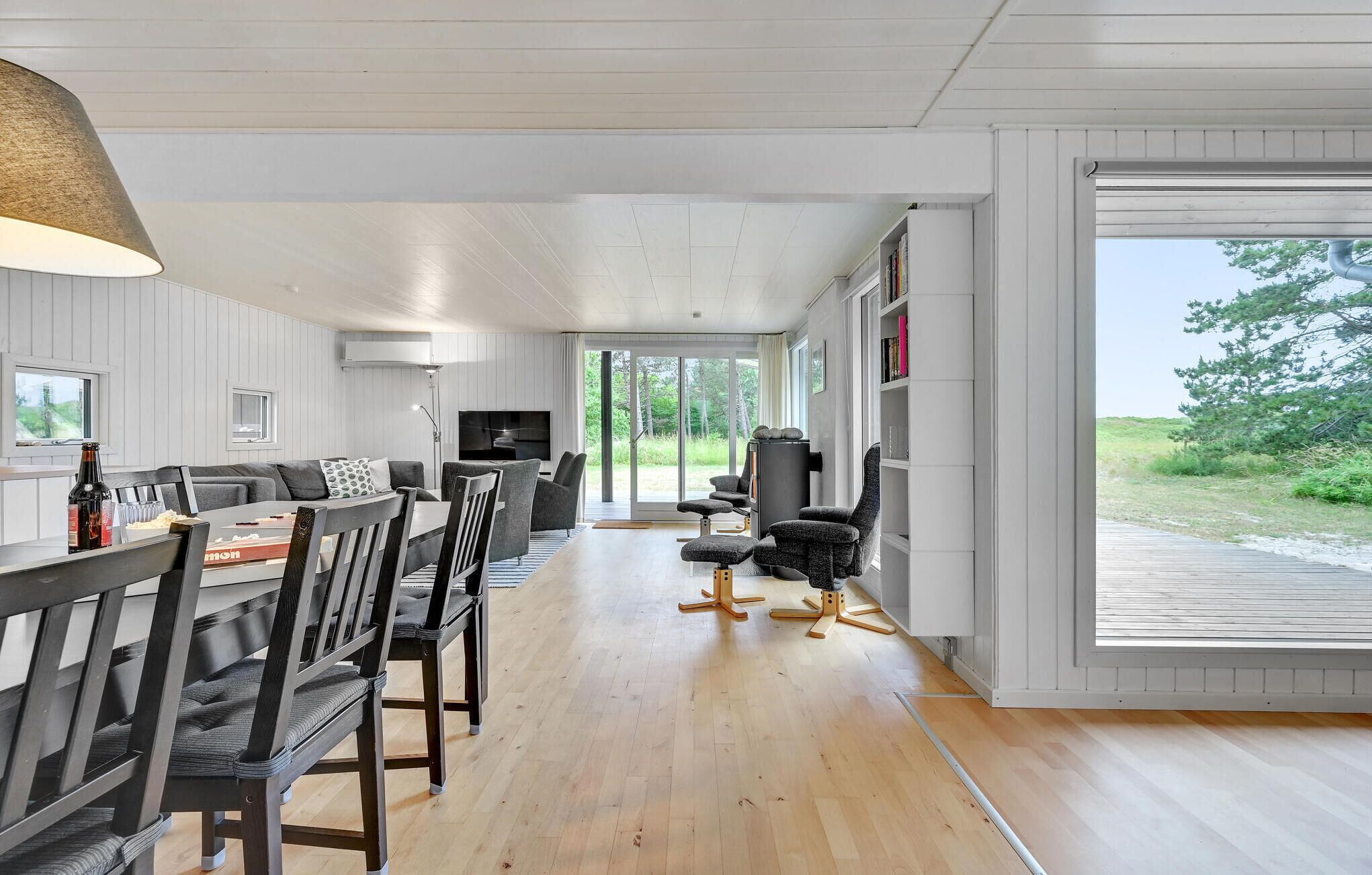 A modern living room with a sofa, dining table, and chairs, a TV, and a bookshelf.