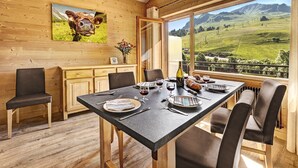 A dining area with a table set for four, wooden cabinets, and a large window with a view of a green landscape. - Beautiful, bright 3 rooms flat for 5/7 people (Le Grand-Bornand)