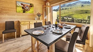 A dining area with a table set for four, wooden cabinets, and a large window with a view of a green landscape.