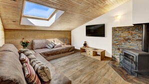 A cozy loft-style living room with a wooden ceiling, a stone fireplace, and a large window. - Beautiful, bright 3 rooms flat for 5/7 people (Le Grand-Bornand)