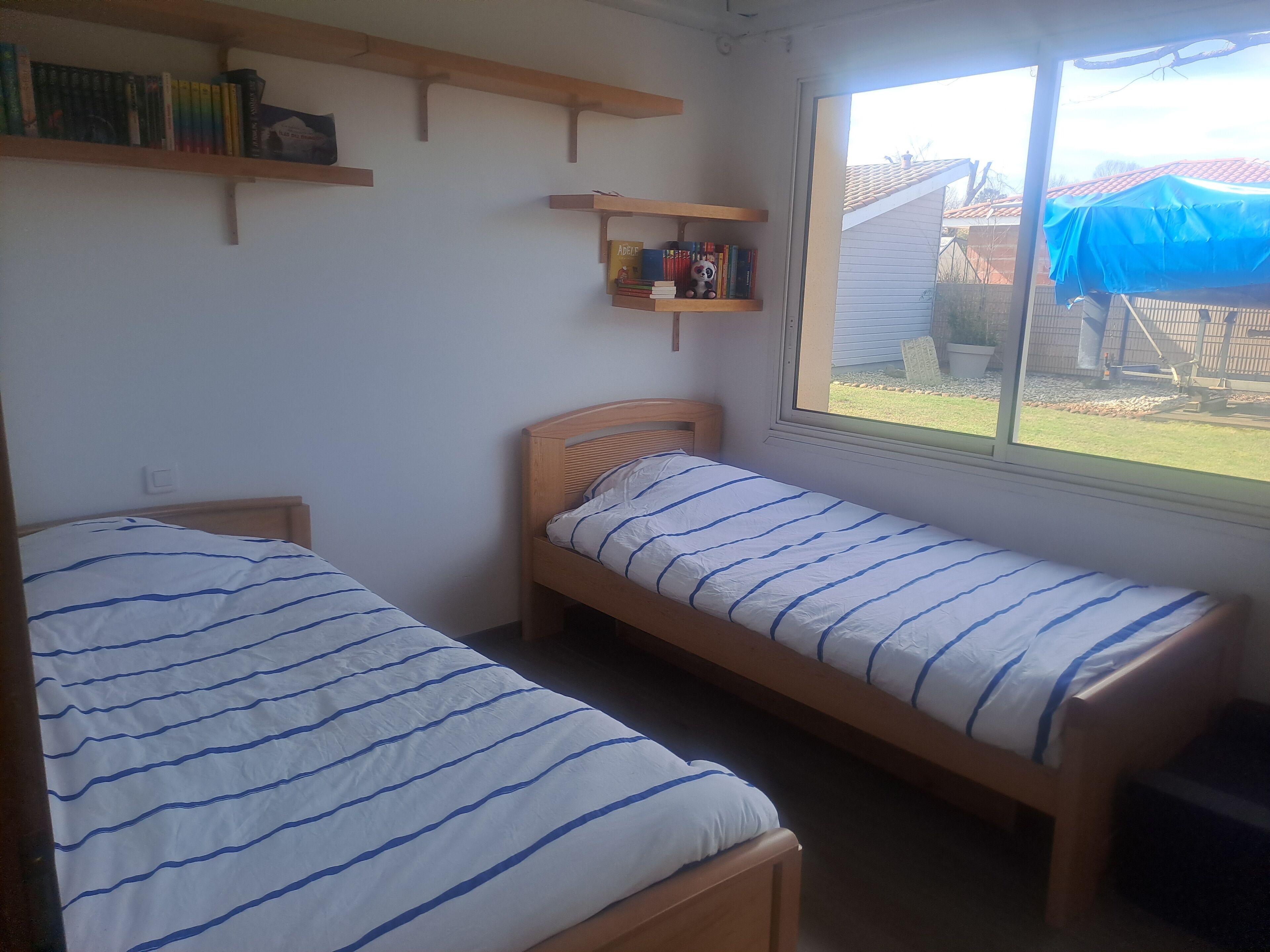 Ein kleines Zimmer mit zwei Einzelbetten, Holz-Kopfteilen und einem Fenster mit Blick auf einen Innenhof.