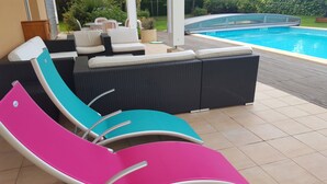 Zona junto a la piscina con muebles de mimbre y sillones de colores vivos.