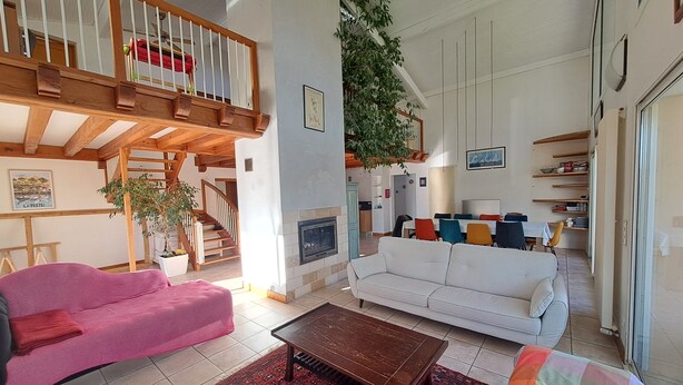 Amplia sala de estar con escalera, chimenea y comedor.