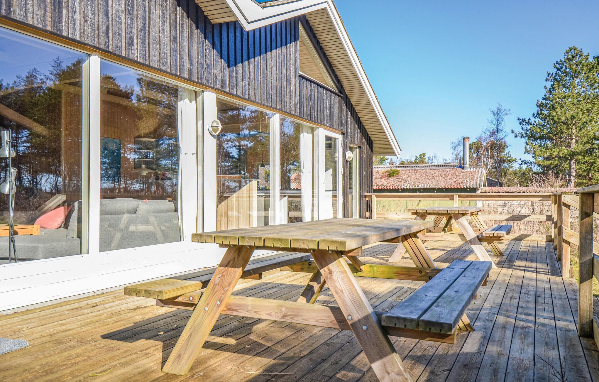 A wooden deck with picnic tables and a glass-enclosed room with a sofa and cushions.