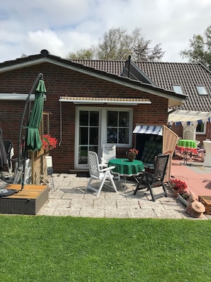 Un espace patio avec une table et des chaises couvertes, un parasol vert et une maison en briques avec un toit en tuiles.