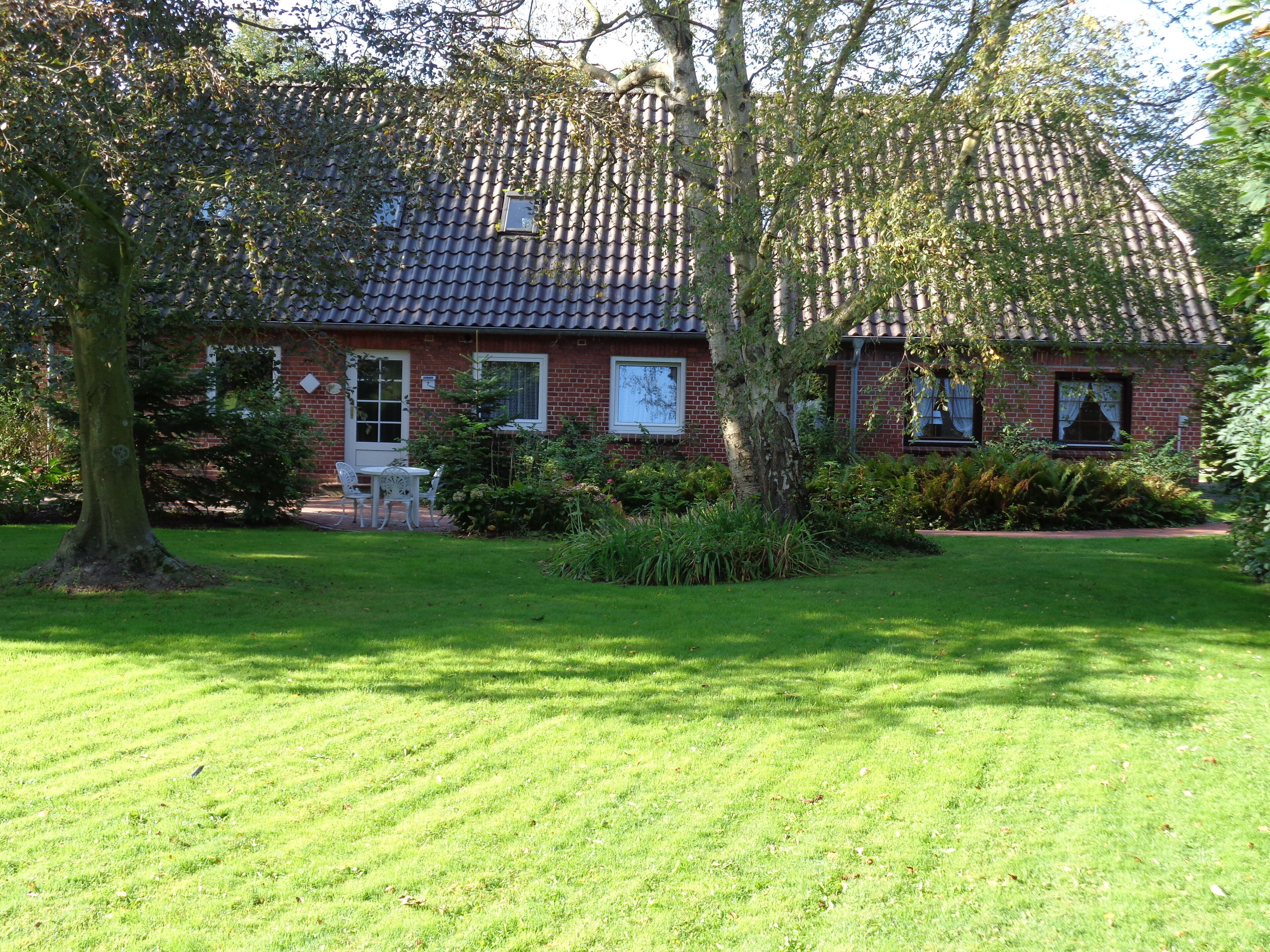 A brick house with a tiled roof, surrounded by a well-maintained lawn and trees.