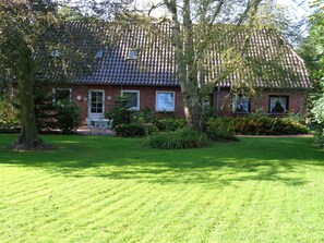 Une maison en briques avec un toit en tuiles, entourée d’une pelouse bien entretenue et d’arbres.