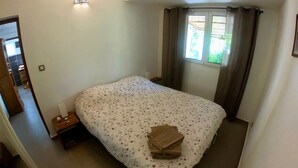 A bedroom with a bed, a nightstand, a window with curtains, and a door leading to another room. - Le Veloutier: Between sea, mountain and volcano (l'Étang-Salé les Bains)