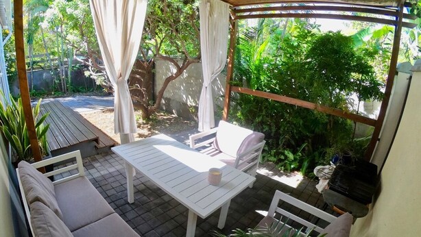 A covered patio with a white table and chairs, surrounded by lush greenery. - Le Veloutier: Between sea, mountain and volcano (l'Étang-Salé les Bains)