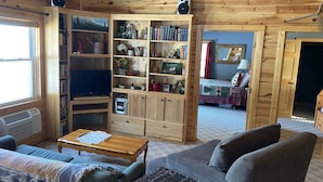 A cozy living room with a wooden bookshelf, a television, and a comfortable seating area. - YEAR-ROUND Private, Cozy Lakeside Cabin. Beautiful Views, 2 Boats, Kayak & Canoe (Ironton)