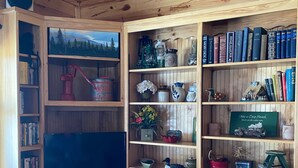 A wooden-paneled room with a television, bookshelves, and various decorative items. - YEAR-ROUND Private, Cozy Lakeside Cabin. Beautiful Views, 2 Boats, Kayak & Canoe (Ironton)