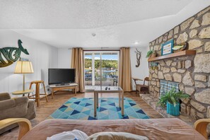 A room with a television, a dining table, a sofa, and a stone wall.