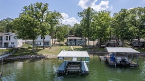 A lakeside property with a dock, a covered boat house, and a house with a porch.