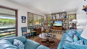 A spacious living room with a stone fireplace, a large TV, and a view of a lake.