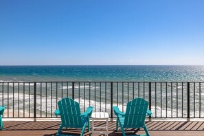 Terras met twee groene Adirondack stoelen en een tafeltje, met uitzicht op een strand met helderblauw water en een metalen hekwerk.