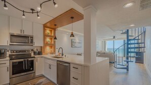 Una cucina moderna con elettrodomestici in acciaio inossidabile, un muro decorativo in legno e vista sull'area soggiorno con una scala.