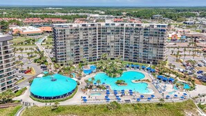 Un hotel di grandi dimensioni con numerosi balconi, una piscina centrale e una zona piscina curata con lettini.