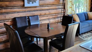 Interior de uma cabana de madeira com uma mesa de jantar, cadeiras, um sofá e um quadro na parede.