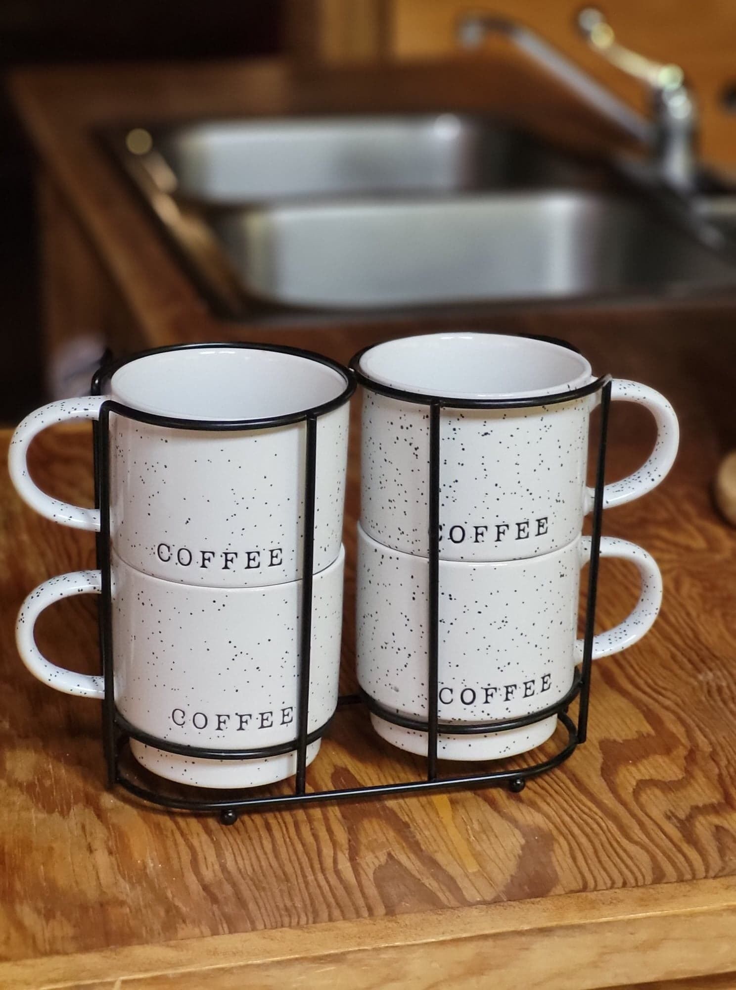 Two white mugs with black speckles and the word 'COFFEE' on a metal rack.