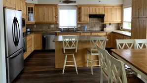 A modern kitchen with wooden cabinets, a stainless steel refrigerator, a dishwasher, and a bar area with stools.