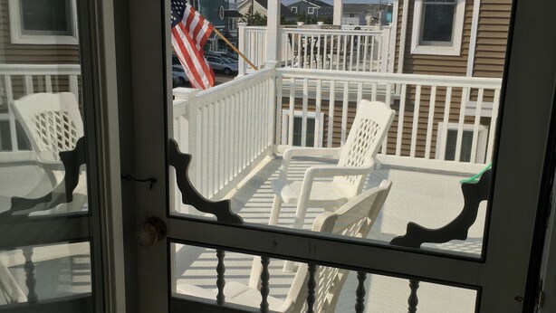 A view through a door of a deck with white chairs and a white railing.