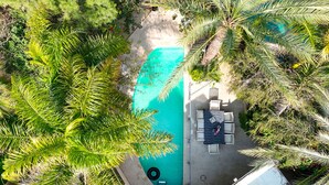 An aerial view of a swimming pool surrounded by lush greenery, with a seating area and a small deck.