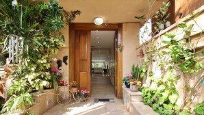 A narrow pathway leading to a wooden door, flanked by potted plants and a metal bicycle.