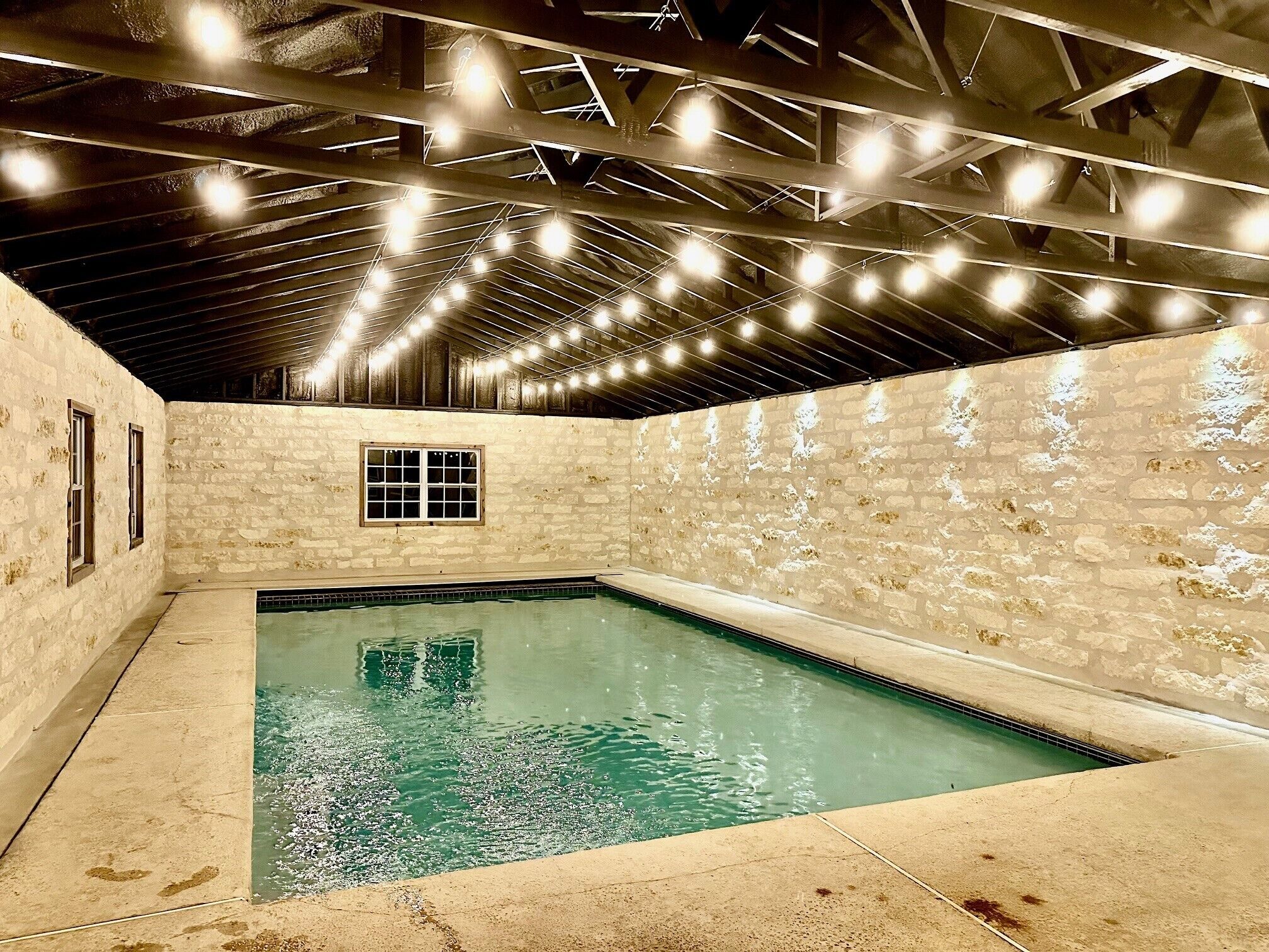 Une piscine intérieure aux murs en pierre et au plafond haut, avec des poutres apparentes.