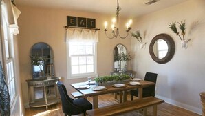 Een eetgedeelte met een houten tafel gedekt voor vier personen, een kroonluchter en decoratieve wandelementen.
