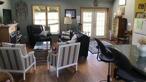 Un vaste espace de vie doté d’une grande fenêtre, d’un canapé en cuir noir, d’un fauteuil blanc et d’une table à manger avec des chaises.