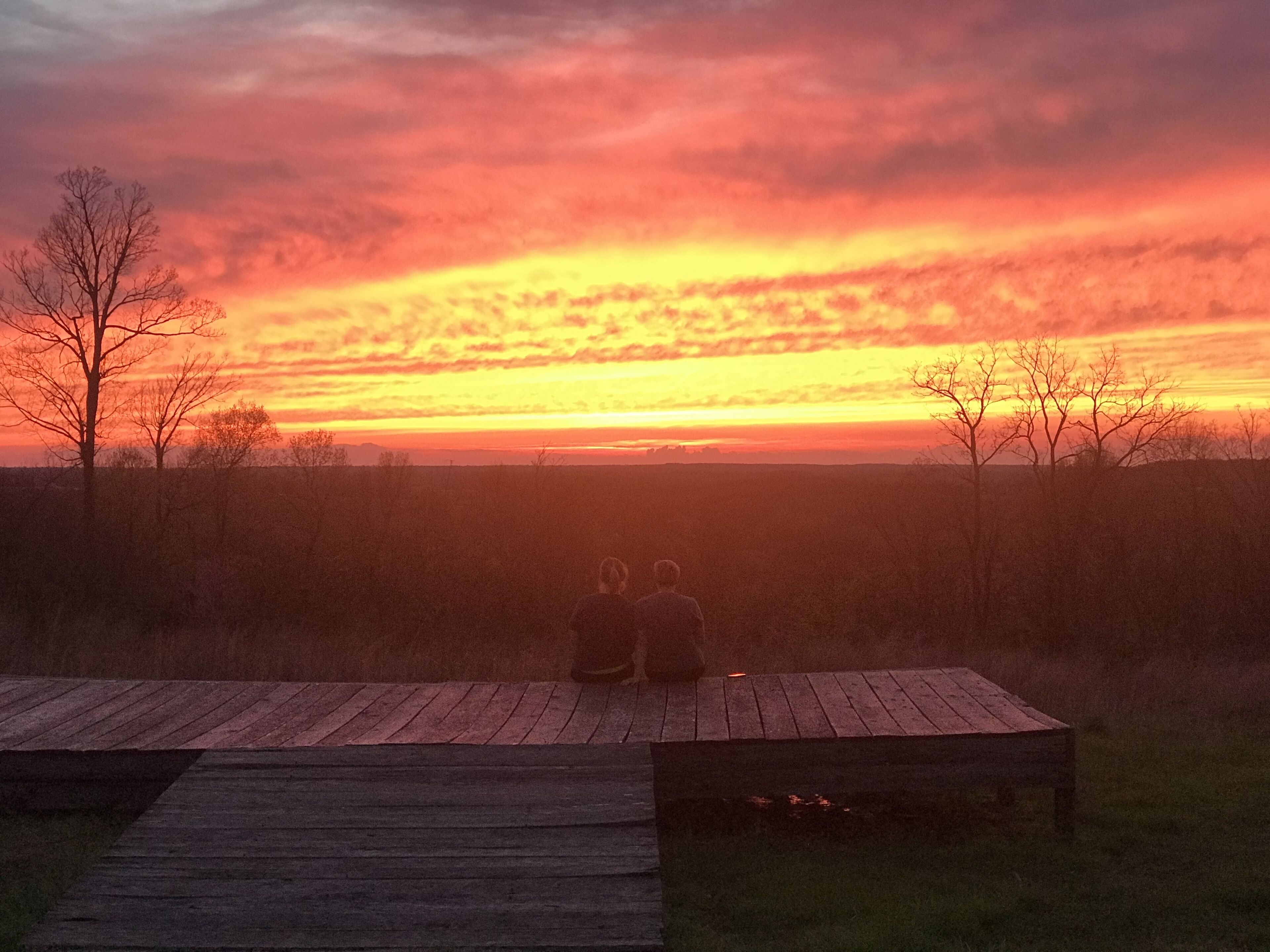 Two people sitting on a wooden bench overlooking a sunset.