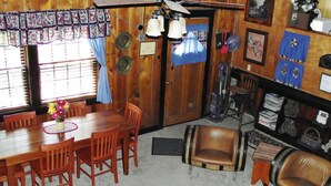 A dining area with a wooden table and chairs, a vase of flowers, and a window with blinds. - Pine Crest- Historic 3 bedroom Log Cabin built in the 1930's by the CCC.   (Custer)
