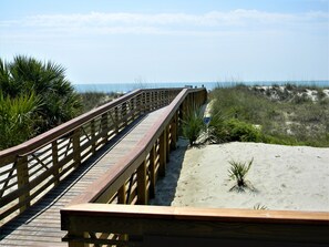A wooden boardwalk leading to a beach with sand dunes and sparse vegetation.
