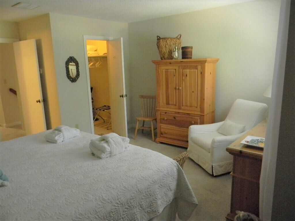 Ein Schlafzimmer mit einem großen Bett, einem Holzschrank, einem weißen Sessel und einem Stuhl.
