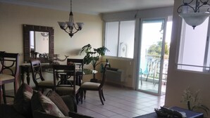 A spacious living room with a sofa, dining table, chairs, and a large window with a view.