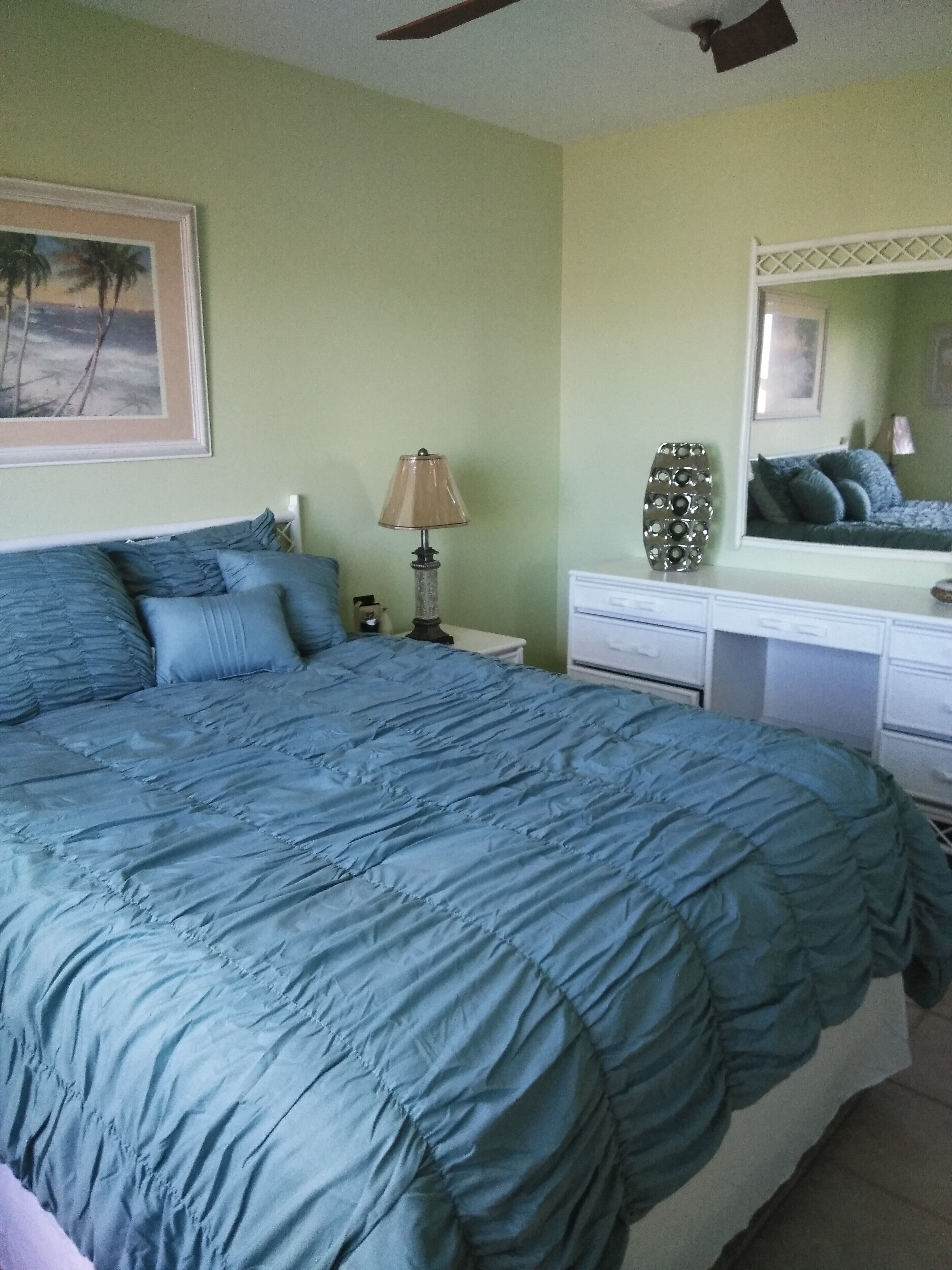 A bedroom with a large bed, a nightstand, a lamp, a dresser, and a mirror.