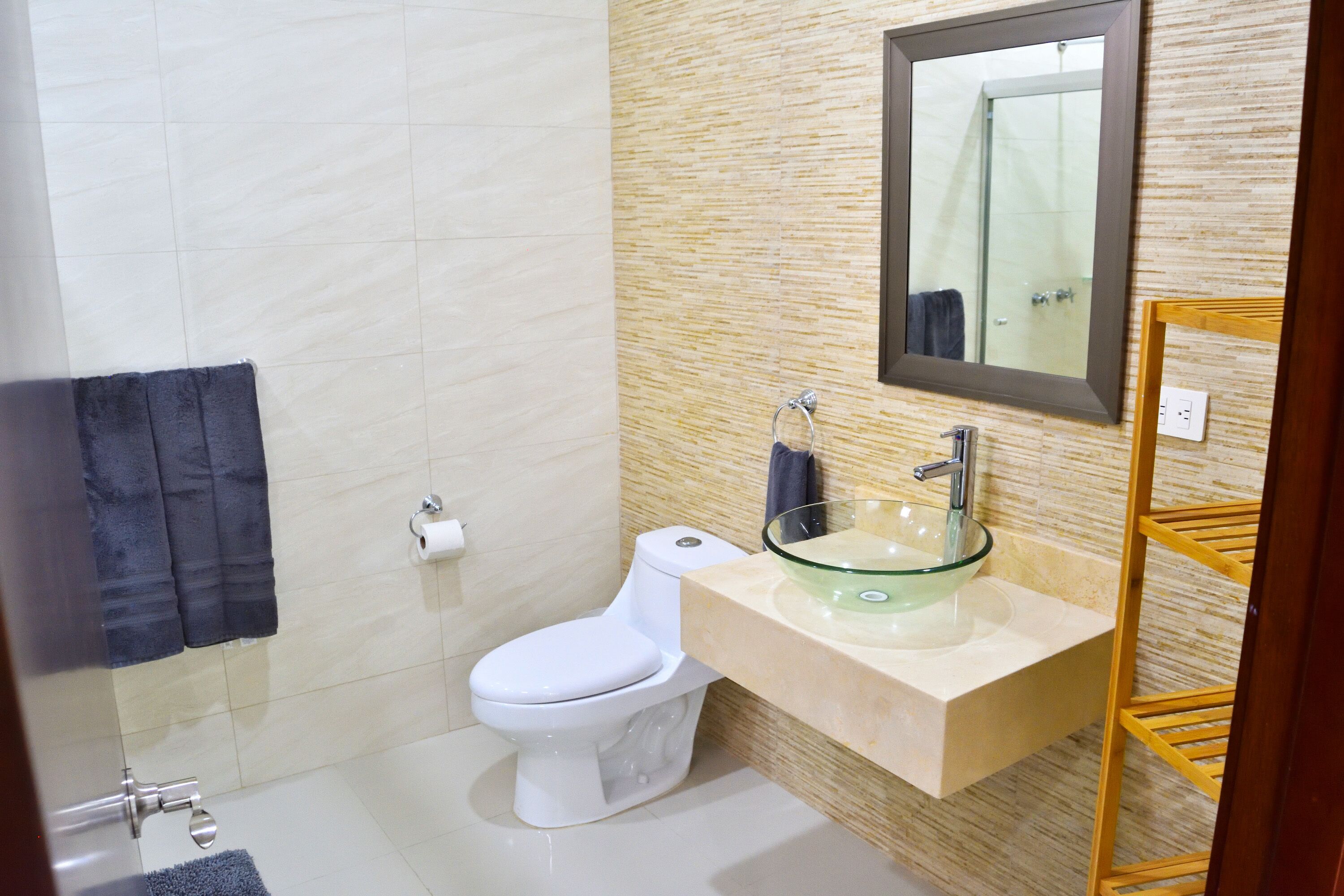 A modern bathroom with a white toilet, a glass sink, and a wooden shelf.