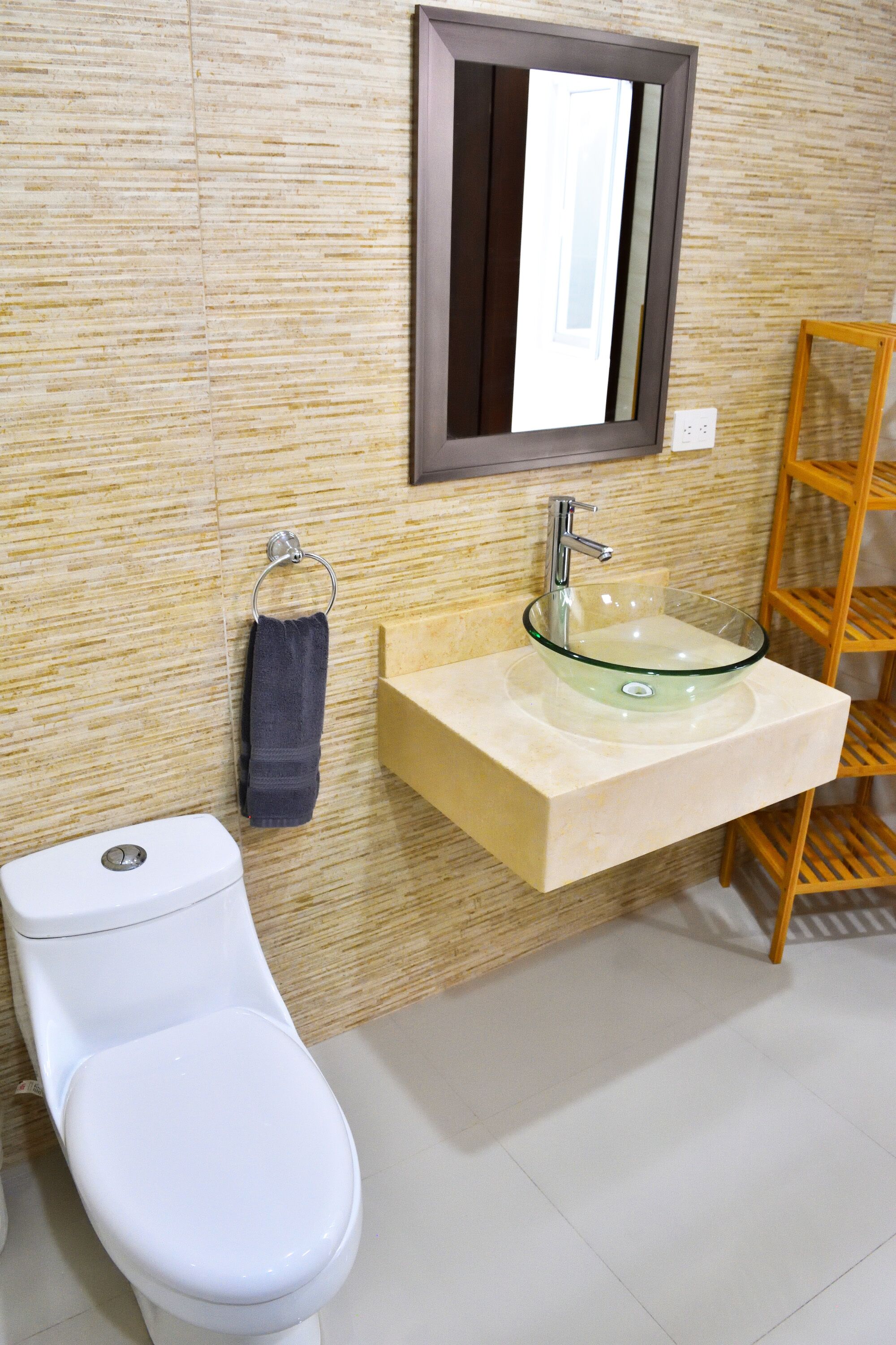 Un baño con inodoro blanco, lavabo de vidrio, estante de madera y espejo en la pared.