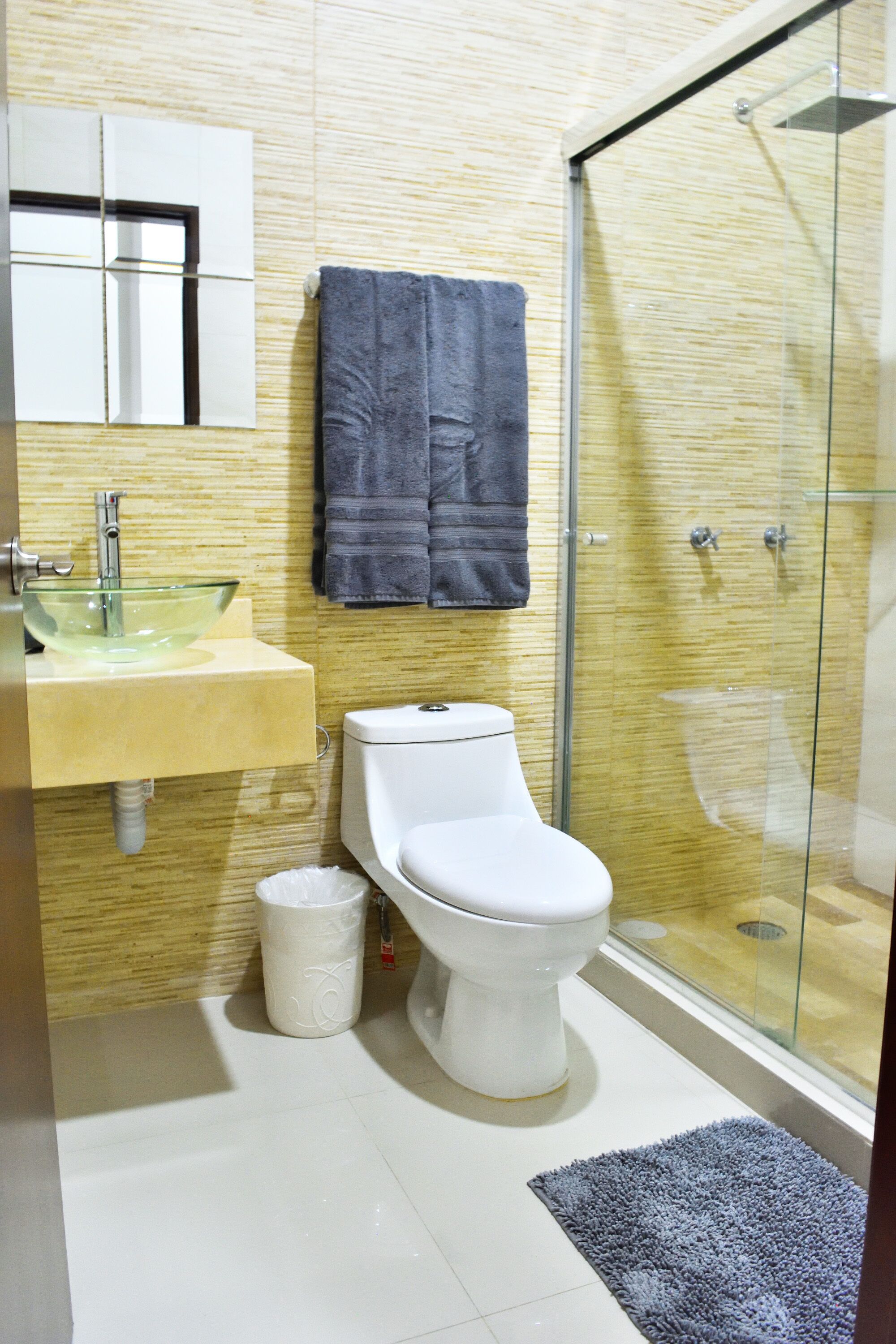 Une salle de bain avec une douche à parois de verre, des toilettes, un lavabo avec un récipient en verre et une serviette accrochée au mur.