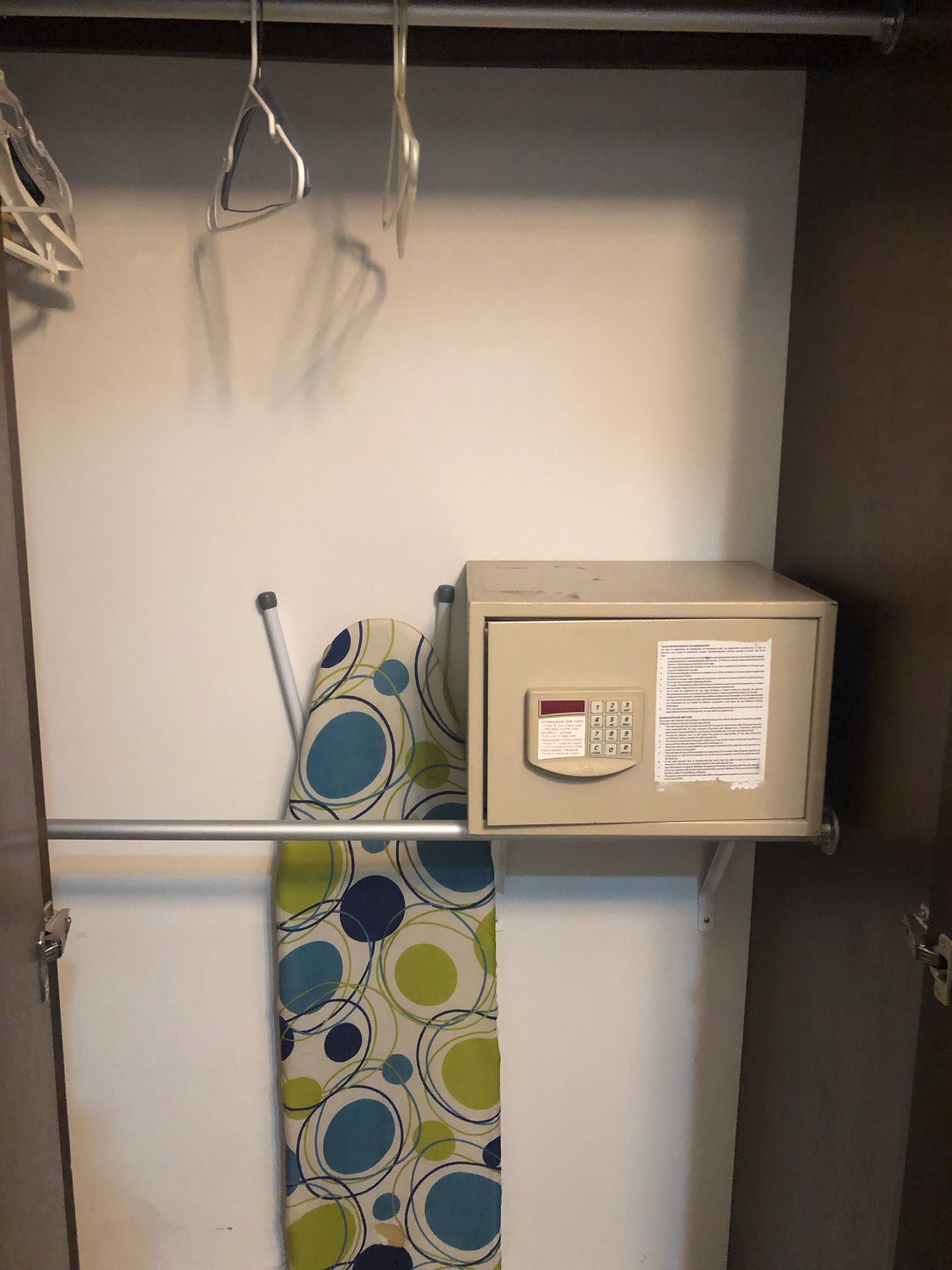 Un espace de rangement comprenant un classeur beige, un rideau à motifs et une étagère en métal avec des cintres.