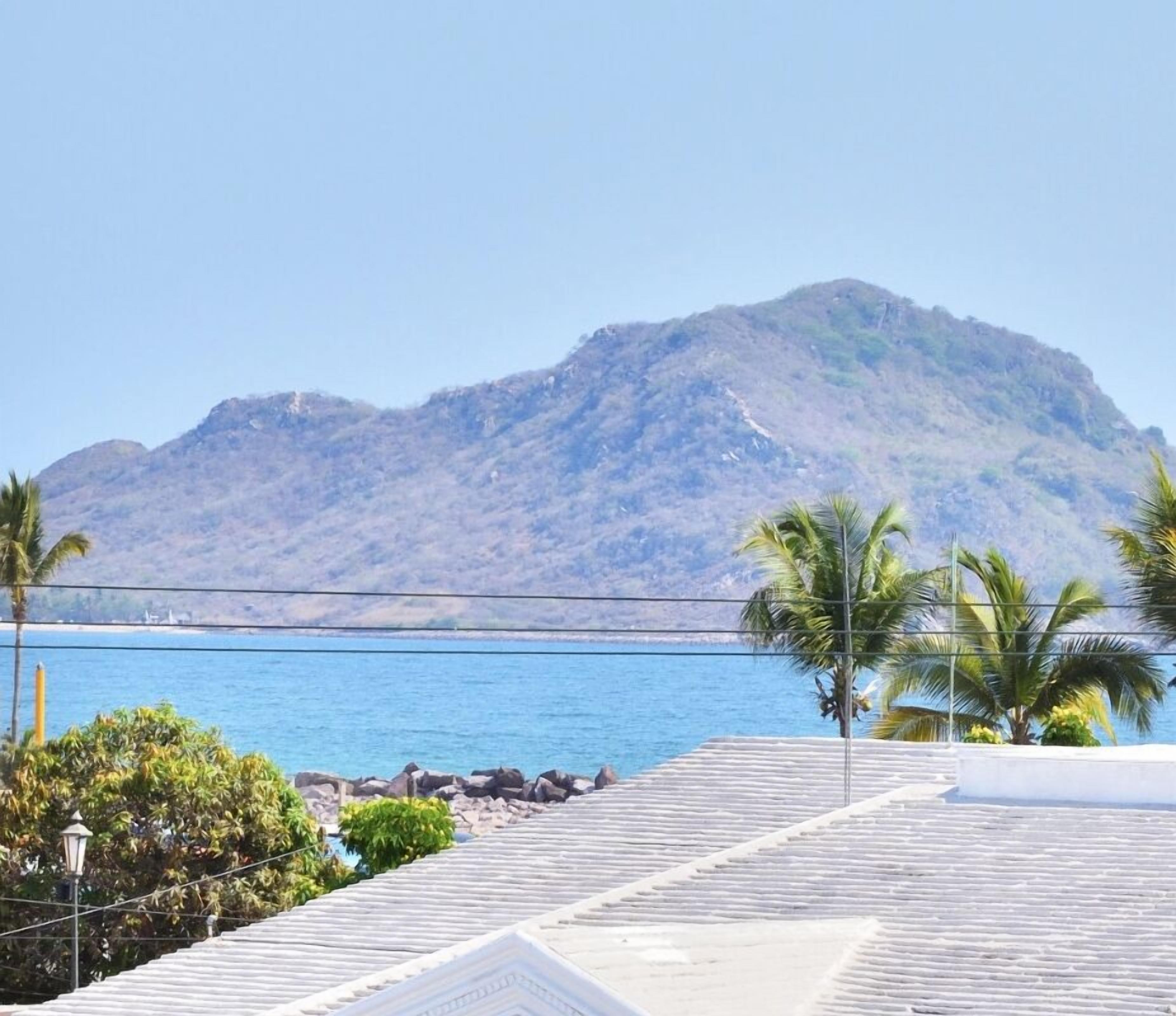 Eine Küstenansicht, im Hintergrund ein Berg, klarer Himmel und ruhiges Meer.
