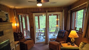 A cozy cabin interior with a fireplace, two armchairs, a sofa, and a table with a lamp. - A Perfect Northern Get-Away On The Scenic Big Creek In Luzerne (Luzerne)