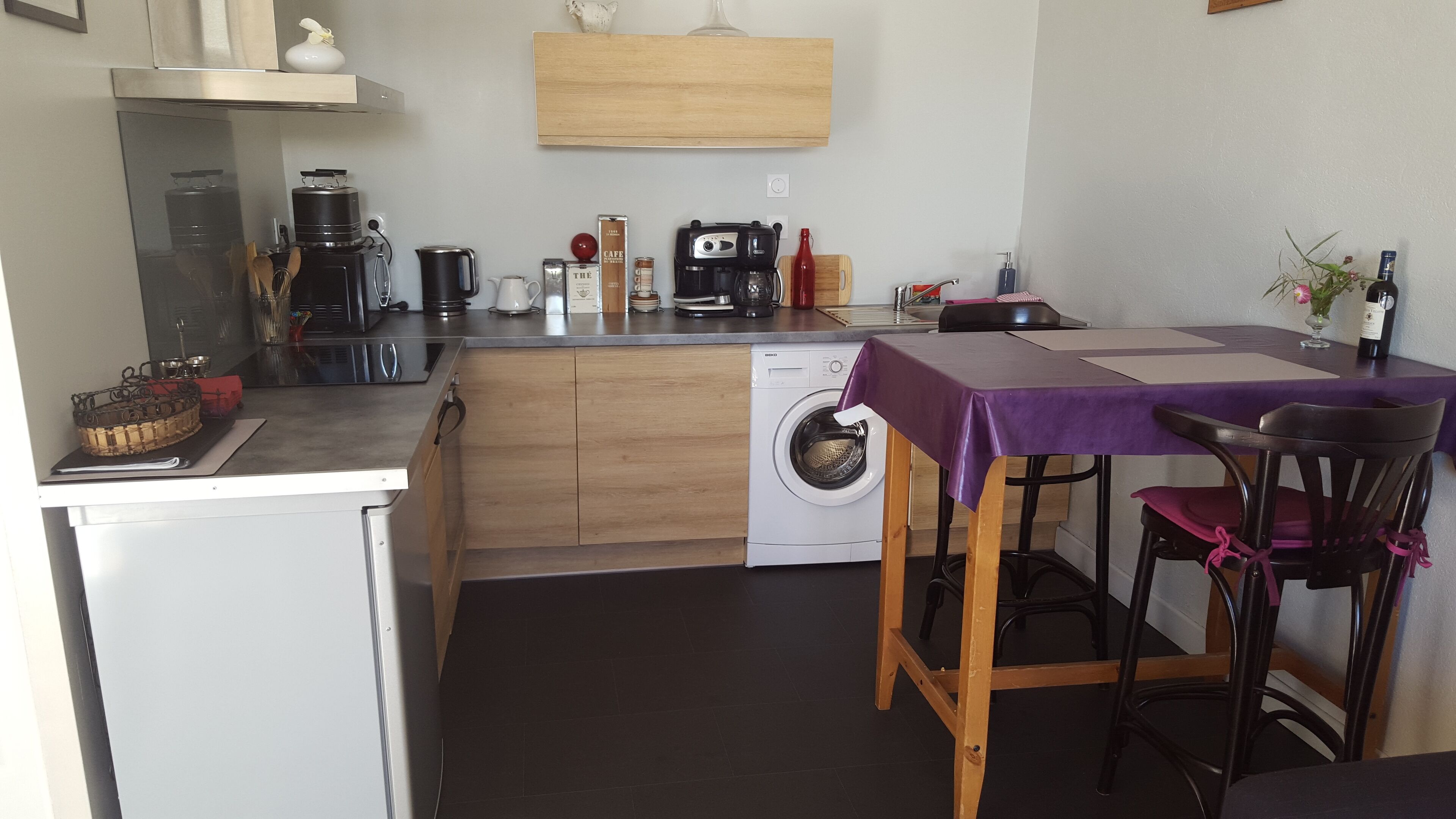 A compact kitchen with a washing machine, a coffee maker, and a dining area with a table and chairs.