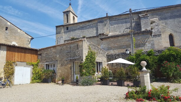 Une cour bordée de bâtiments en pierre, un clocher et un chemin de gravier.