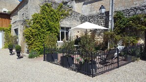 Une cour avec un bâtiment en pierre, une clôture en fer forgé noir et des plantes en pot.